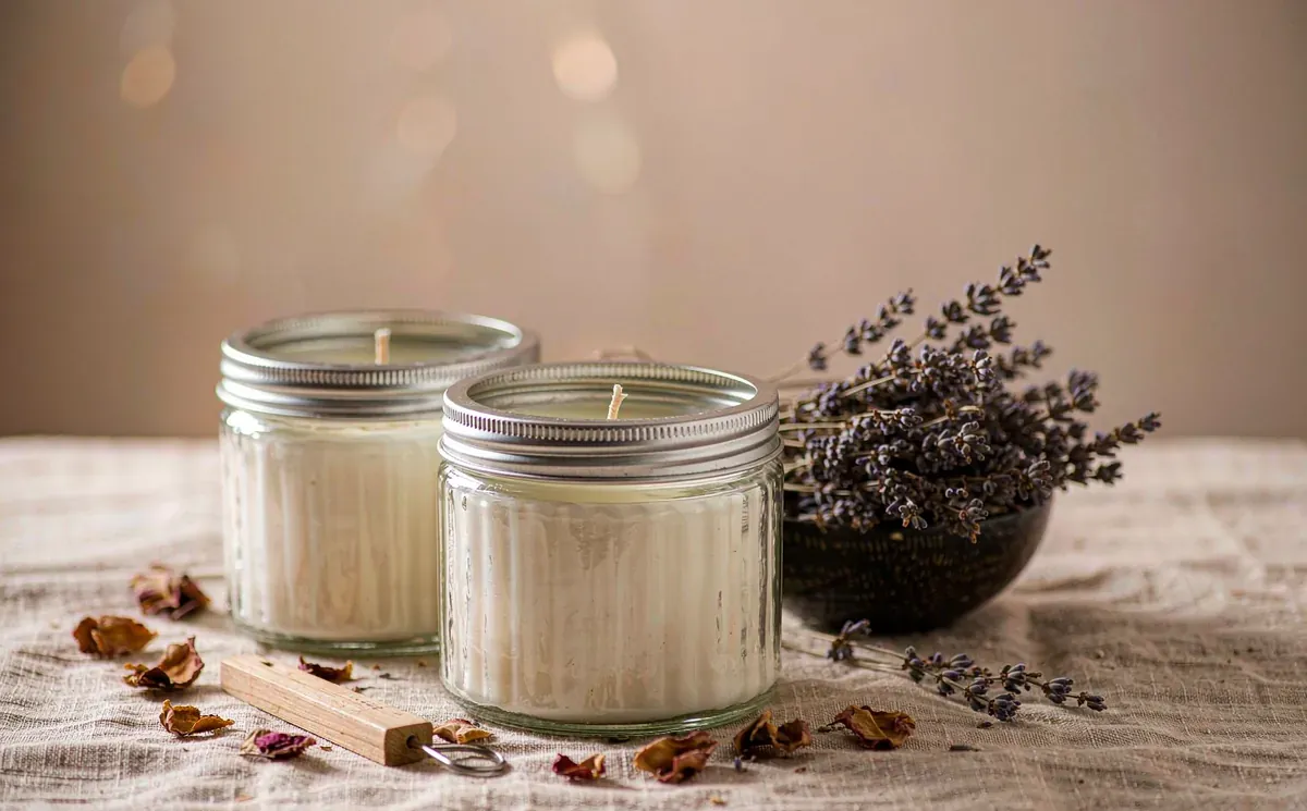 Artisan scented candles in glass jars with dried botanicals on a linen cloth